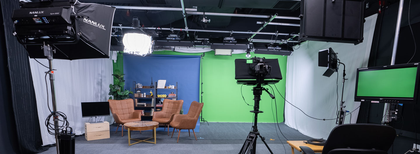 Photo of video studio with an interview setup and a green wall with lights and camera equipment in the foreground