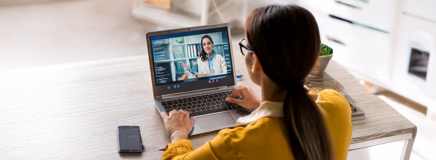 Photo of a person looking at a laptop screen with a presenter teaching an online lesson